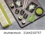Small photo of Nori sushi, wasabi in a bowl, rice on nori sheet. Bamboo mats. Flat lay. Dark background