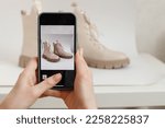 Small photo of A woman takes a picture of new shoes on a mobile phone at home. Mobile shooting for goods for sale. Blogger and stylist photographing clothes. Reusing unnecessary things