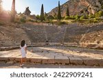 Small photo of Greek history: A long-haired woman from behind, wearing white dress looking at Apollo Temple and Ancient Theater in sunset. Delphi, Greece.