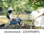 Small photo of Camping outdoor. Asian women camping leisure and destination travel near waterfall. People hand holding smartphone and drinking coffee on the tents in morning. Tourism relax and chill summer holiday