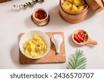 Small photo of Pangsit chili oil, Pangsit dower, or chili oil spicy dumplings served on white bowl, cutting board, steamed bamboo , soup spoon, chili oil, and chili. Indonesian snack, jajanan viral.