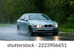 Small photo of Stony Stratford,Bucks,UK - November 8th 2022. 1998 BMW 523 classic car driving in the rain on a wet road