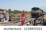 Small photo of Tiruppur, India - March 8, 2018: A train on the southern section of Indian railways approaching a road crossing. The rail network extends to 75,000 miles of track and transports 23m passengers daily