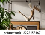 Small photo of Pilates fitness trainer doing exercises on in pilates studio. Reformer pilates studio machine for fitness workouts in gym. Fit, healthy and strong authentical body. Fitness concept