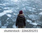 A single woman overlooks a partially frozen river during the winter time.