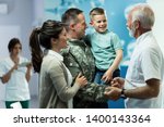 Happy senior doctor talking to little boy who came with mother and military father at clinic. Focus is on military man. 