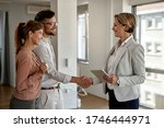 Happy real estate agent and young couple shaking hands after successful agreement. 
