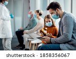 Father and daughter wearing protective face masks while surfing the net on digital tablet in a hallway at the hospital. 