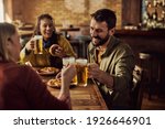 Group of happy friends toasting with beer while having lunch in a pub. Focus is on man. 