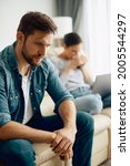 Small photo of Distraught man sitting on the sofa and thinking while having relationship problems with his wife at home.