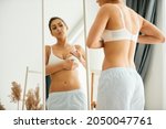 Young woman doing breast self-examination while looking herself in a mirror at home.