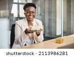 Happy African American businesswoman holding cake with lightened candle in the office and looking at camera. 