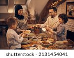 Happy Muslim parents and their kids sharing pita bread while eating dinner on Ramadan at home. 