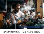 Young happy barmen preparing mojito cocktail and adding mint leaf in a glass at bar counter.