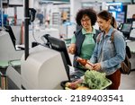Young happy woman using self-service checkout with help of supermarket worker. 