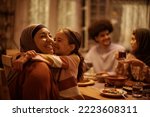 Small photo of Affectionate Muslim grandmother and granddaughter embracing during family meal in dining room.