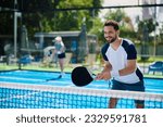 Small photo of Happy athletic man standing by the net while playing padel with friends on outdoor tennis court.