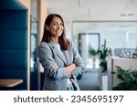 Young happy businesswoman with arms crossed standing int he office and looking at camera.