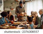 Small photo of Happy African American man serving traditional roast turkey while gathering with his family for Thanksgiving at dining table.