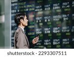 Small photo of See the stock price board reflected on an outdoor electronic bulletin board with a smartphone in your hand, a man in a suit in his thirties in his thirties