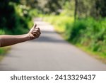 Small photo of A lone figure stands by a quiet village road, thumb extended in a silent plea for a ride