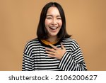 Small photo of Portrait of extremely happy girl holding hand at her chest and laughing out loud, chuckling giggling at amusing anecdote, sincere emotion. Indoor studio shot isolated on beige background