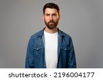 Small photo of Portrait of attentive self confident bearded man looking at camera with serious expression, unsmiling determined business man. Indoor studio shot isolated on grey background