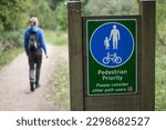 A person walks along a trail in the park passed a sign showing pedestrian priority in London UK