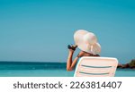 Small photo of Wealthy woman relaxing on the beach, holding her hat and glasses