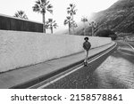 African american man riding longboard on the road with palm trees in background - Focus on face - Black and white editing