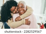 Small photo of African daughter hugging her mum indoors at home - Main focus on senior mother face - Mom day and family love concept