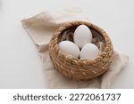 White eggs in brown basket on white cloth
