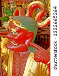 Small photo of Singapore February. Close up of grotesque caricatured red smiley face of deity in Chinese Temple. Gold robe, green hat, wriggly serpent in rear. Finger pointing. Red vest.