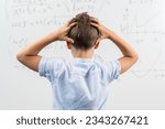 Small photo of View from the back of schoolboy standing in class against blackboard. Boy holding hands on head. Portrait of shocked and emotional little kid. Back to school. Failing to solve a mathematical equation