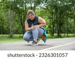Small photo of Overweight young woman with knee pain grabs her knee with both hands while sitting down at a running track of a local park