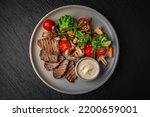 Small photo of Hearty, dietary dish. Salad with beef, vegetables and tuna sauce in a ceramic plate on a dark textured background. Restaurant menu Isolated on black