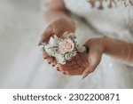 Wedding details. The bride holds the groom's wedding boutonniere. hands folded in the shape of a heart. Beautiful hands. French manicure