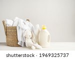 A basket of white laundry, a teddy bunny toy, a bottle of liquid detergent, washing gel or fabric softener. Mockup for washing baby clothes with copy space.