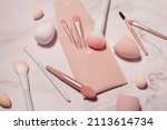 Small photo of Makeup artist's tools in pink on a marble dressing table: brushes for powder, blush, eyebrows, shadows and sponges for concealer and foundation.