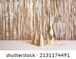 Small photo of A bottle of champagne, glasses and party hats are on the table against the backdrop of a golden tinsel curtain.