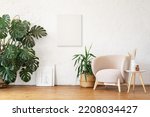 Small photo of White canvas mockup for poster or lettering. A cozy modern beige armchair against the background of a white empty wall. Interior mockup with copy space.