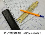 Small photo of A vintage slide rule lies on the table among pieces of paper with examples of mathematical calculations. Retro device for mathematical calculations.