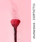 Small photo of close-up on a blush brush with pink blush crumbling on top on a pink background