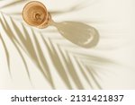 Small photo of White wine glass peach color glass on beige background with palm leaf shadow, glare at sun. Minimal summer rest concept. Dry wine in colored glassware goblets style. Creative top view, pastel colors