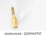 Top view white sparkling wine bottle with sunshine long shadow and flare on light white background. Minimal aesthetic flat lay, one champagne bottle with golden foil. Summer alcohol drinks, copyspace