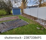 Small photo of A backyard lawn smothering project in progress, with tarps pulled away to dry and dead grass in the project area