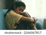 Small photo of Unhappy girl portrait, Sad child sitting on sofa at home, Upset girl hugging knees alone, Concept of lonely girl and kid with trouble and violence