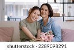 Small photo of Happy time Mother day grown up child girl looking at camera cuddle hug give flower bouquet gift to mature mum. Love kiss care mom asia middle age adult people smile enjoy relax sitting at home sofa.