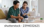 Small photo of Young married asia people prepare pregnant plan preconception drug at home sofa. Health care unbox open Rx mail parcel covid first aid kit box self cure buy pill order online by clinic service store.