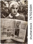 Small photo of UKRAINE, USSR - CIRCA 1960: A pretty young girl sitting and reading the newspaper Komsomolskaya Pravda (Komsomol Truth) at summer day outside